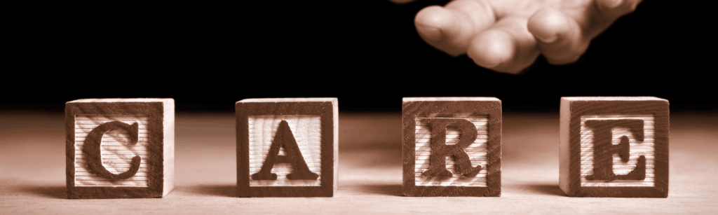 Sepia-toned image of children's toy blocks spelling out the word "care" with a hand extended from the darkness behind it.