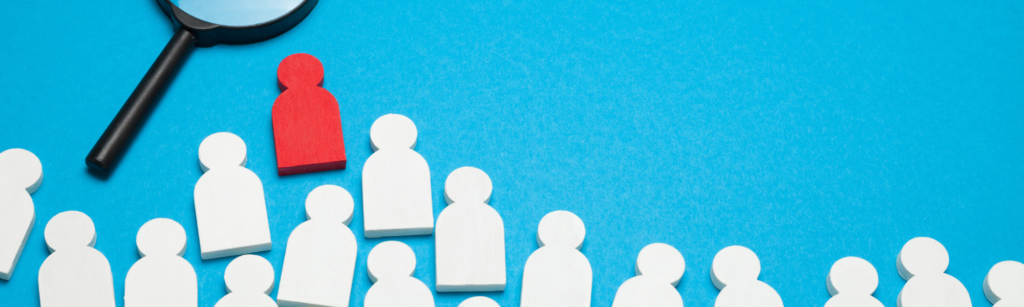 A magnifying glass above cutouts of generic bust-shaped profiles. all of the profiles are white, except for one that is bright red, standing out and rising above the rest.